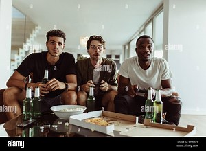 Friends having fun with drinks and snacks while playing video game at home. Two men playing video game holding joysticks while another man watches wit Stock Photo - Alamy