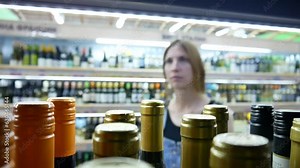 Many glass wine bottles in a liquor store close-up and a young woman chooses one