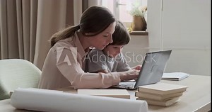 Cheerful preschool boy playing and fooling around with computer, and mother young woman trying to teach him how to type and learn online using a laptop. New technology and children.