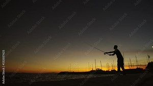 Young fisherman fishing by the seashore in slow-motion, throwing fishing rod in sea at sunset