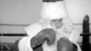 Muscular man in Santa Claus suit with boxing gloves trains in the ring.