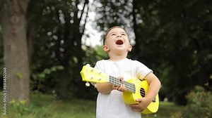 Happy little boy playing on the guitar in the park