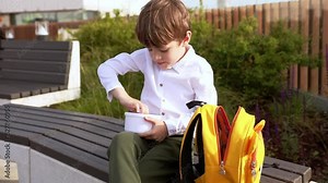 First grade school boy sits outside and opens vegetable lunch