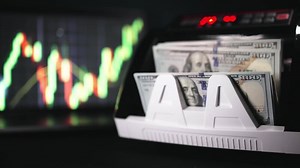 Electronic money counter machine counts American one hundred dollar banknotes. Finance and banking concept. Financial figures and diagrams showing changing price.