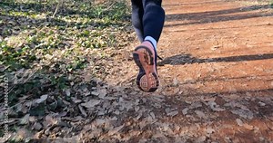 Running female legs in sneakers. Closeup view of fitness woman legs in sports shoe jogging in the forest. Back view. Slow motion.