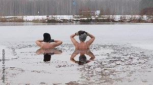 Two young, beautiful women take an ice bath in a frozen lake, surrounded by snow-covered nature. The icy water providing a refreshing and invigorating experience during winter swimming