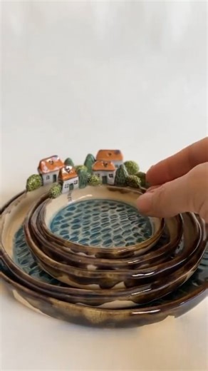 Love in Pottery on Instagram: "Mila (@milushka_mila) is a ceramic artist based in Croatia, known for her whimsical storytelling through clay. With a background in painting, illustration, and traditional crafts, she now focuses on creating one-of-a-kind ceramic art pieces that feel like miniature fairy tales. Milushka showcases a charming collection of handbuilt ceramic plates that capture the essence of a tiny Mediterranean village. Each piece features pebble-textured blue “sea” centers and deli