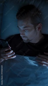 Top view, young man laying in bed at night, holding smartphone and doom scrolling through social media, then tossing the phone aside in exhaustion and frustration. Smartphone addiction. vertical video