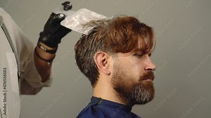 Hair salon, hair coloring man. Process of a guy having his hair dyed at hairdresser. Beauty and people concept. Stylist man with hair dye and brush coloring hair at salon.