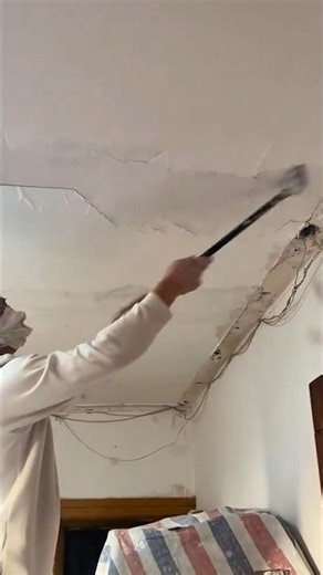 scraping old plaster and paint from the ceiling with a long handled metal scraper tool