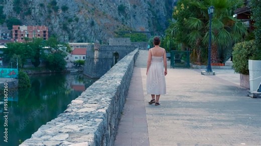 Elegant woman walking on the kotor fortress walls in montenegro. Following shot of a beautiful young woman in a summer dress walking away along the ancient stone walls of kotor's old town