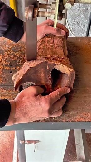 cutting a piece of brown wood log using an electric metal band saw machine