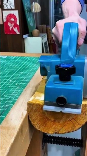 shaping a small wooden block with a blue electric planer to create many wood shavings on cutting mat