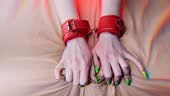 Girl's hands are shackled with red leather handcuffs for role-playing...