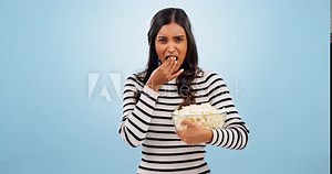 Popcorn, shock and woman in a studio for movie, film or show with entertainment or fun. Surprise, crazy and portrait of young Indian female person eating snack for cinema isolated by blue background.