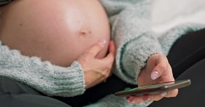 Jeune femme enceinte défilement photos téléphone. surfer sur internet. Une mère attentionnée caresse une enceinte nue