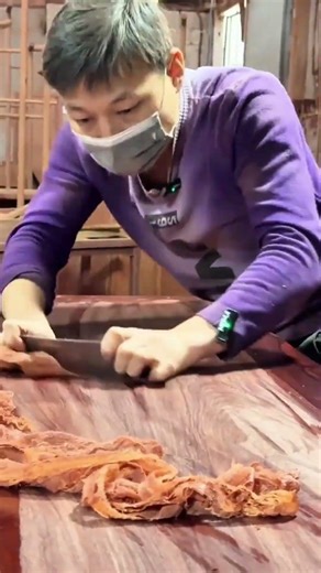 Smoothing the surface of a large wooden table using a hand scraper tool to reveal the natural grain