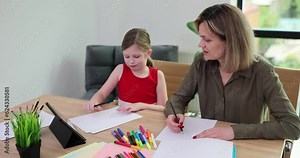 Teacher explains material to schoolgirl during home lesson in living room. Female tutor helps little student with homework printed on school paper