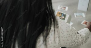 Black woman printing pictures with portable wi-fi mini printer at home. African american people sitting on couch and storing Polaroid prints in photo album. Over the shoulder shot