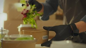 Packing food into biodegradable containers using paper bags and containers, a volunteer works in a modern industrial kitchen. The volunteer organization actively distributes food in organic packaging