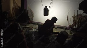 A traditional shadow puppet master playing skillfully behind the white screen.