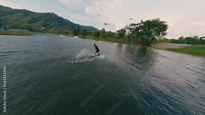 Aerial view sport man riding wakeboarding flat and jibbing tricks slides tropical sunny seascape. FPV sport drone follow shot active extreme male enjoy speed splash ride wakeboard cable jump surf 4k