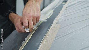 Preparing a car for painting. The car is in the paint booth, parts are cleaned and primed. The painter covers normal parts of the car with a film against paint dusting.