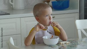Little boy sitting at the dining table and concentrating on eating his lunch at home.