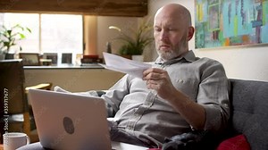 Man looking through his stack of mail, opens up an envelope with a bill and gets stressed out