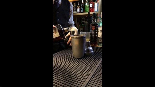 Pouring bright citrus cocktail into curved glass with mint and flower decoration creating elegant drink