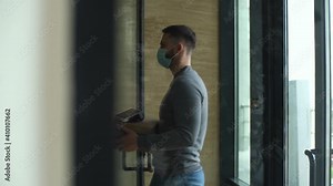 Courier with boxes hot pizza and payment terminal enters lobby of an apartment building. Delivery man in medical mask walks into lobby of office building to meet customer and hand over online order.