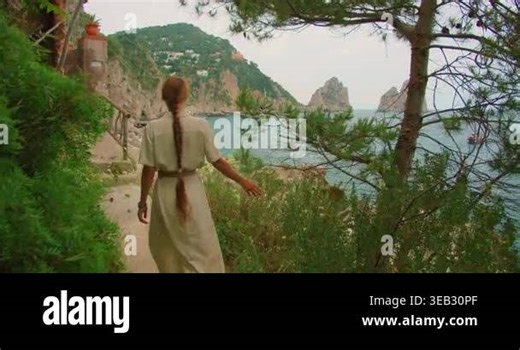 Woman walking along a blooming coastal path towards Faraglioni sea stacks in Capri Stock Video Footage - Alamy