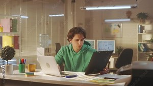 A young man is typing on a computer keyboard, looking at his watch and finishing his working day. A tired manager in a green sweatshirt closes his laptop and wearily rubs his eyes.