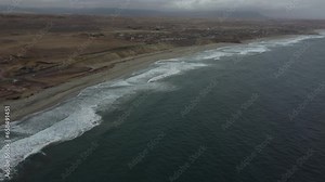 Dark brown Peruvian beach with waves and dark green sea on a misty day