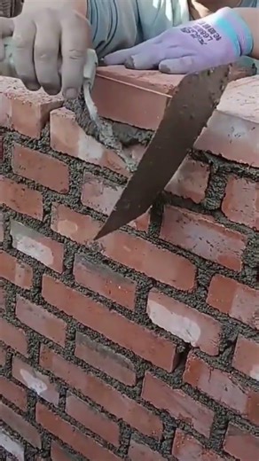 building a tall red brick wall very carefully and neatly using wet grey cement and a metal trowel