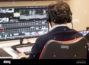 A television director in a broadcast control room, actively guiding a live production. Surrounded by multiple screens, the director wears a headset and gestures towards a video switcher Stock Photo - Alamy