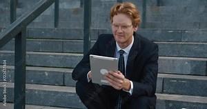 Man in suit sits on steps using tablet for relaxing internet break With tablet in hand he escapes from work rigors browsing content. Enjoying leisure tablet becomes his portal to unwind.