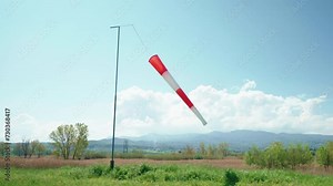 Striped red and white wind sock blowing in wind showing the direction and speed and helping pilot to operate correctly airplane white taking off or landing, wind cone signal or indicator on airfield