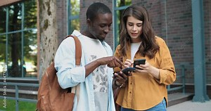 Deep in gadgets. Motion camera view of the diverse classmates standing together at the street during the break and discussing something while looking at the smartphones