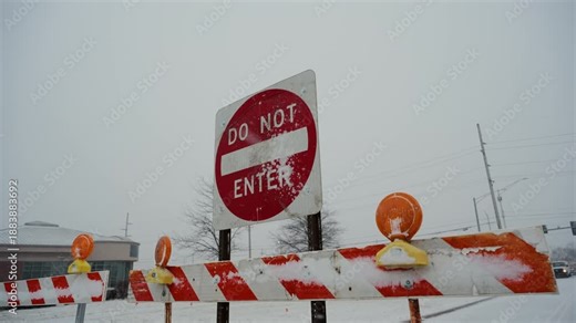 Red Do Not Enter sign stands behind road closure barriers during snowy winter conditions. traffic restriction, blocked access due to weather or road work. Close side POV view