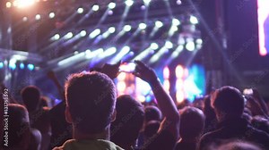 Happy audience applauding to performer on illuminated stage, man filming video