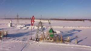 Pump jack in vast oil fields in winter. Pipelines transporting oil from oil pumps, aerial drone shot