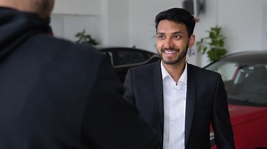 Showroom car, indian sales manager talking to male customer in car dealership showing electric car. Agent