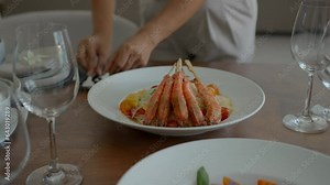 Close-up of woman serving table for dinner, puts plate of delicious meal in centre of table, empty glasses around, dinner party concept