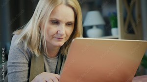 Portrait of a middle-aged woman lying on a bed in her bedroom uses a laptop