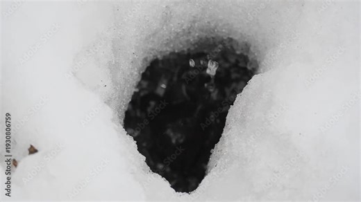 water drops falling into a puddle through a hole in the snow slow motion 180fps. A detailed seasonal sequence capturing the splash and rebound of droplets during a spring thaw