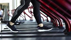 Treadmill in the gym. Side view of legs in sneakers walking on the treadmill in the fitness room. Cardio workout. Girl doing sports. Legs walking on the treadmill at a slow pace, close-up. Sport