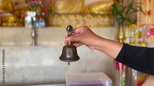 Buddhist bells hanging in temple, Hand ringing small bell inside temple, Buddhist in traditional robes ringing temple bell surrounded by peaceful garden setting