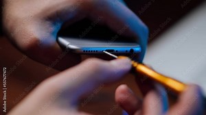 Mobile phone repair in the workshop, hands close-up. A repairman disassembles a smartphone using a screwdriver in a service center. The master unscrews the bolts. Repair and maintenance.