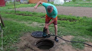 Homeowner pumping sewage waste from septic tank with wastewater pump through maintenance hole.